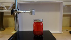Jar filled with a red liquid in front of a white board