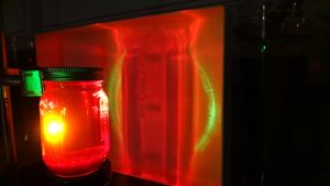 A jar filled with red liquid being struck by a green laser