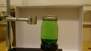 A jar filled with green liquid in front of a white board